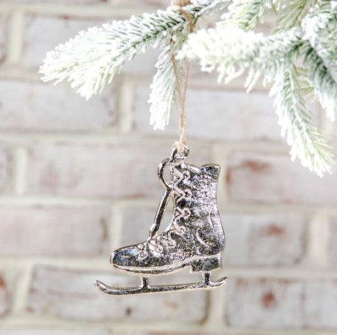 Ice skate ornament hanging on a Christmas tree branch with a white brick wall background