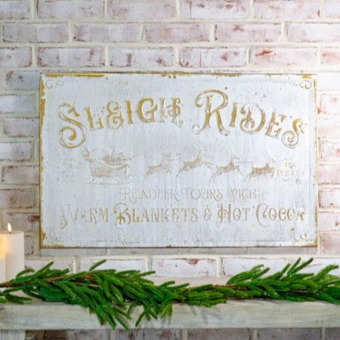 Decorative sign with 'Sleigh Rides' on a brick wall with greenery and candle.