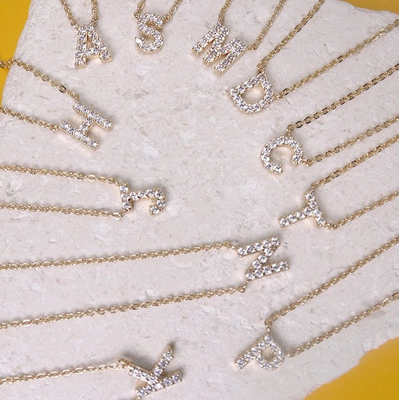 Necklaces with letter pendants on a white stand against a yellow background