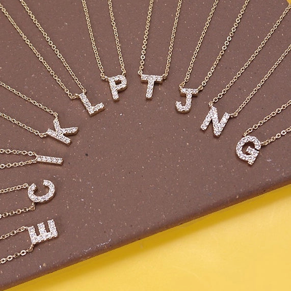 Gold necklaces with letter pendants on a brown and yellow background