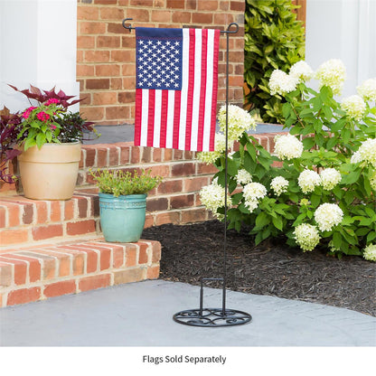 Elegant Swirl Flag Stand Base made of black metal with American flag on a patio with plants and flowers