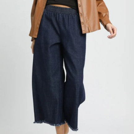 Person wearing dark blue wide-leg pants with a brown jacket on a light gray background