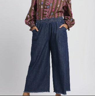 Person wearing a patterned top and blue denim pants on a plain background