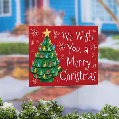 Christmas-themed yard sign with a tree and text in front of a blurred outdoor background.