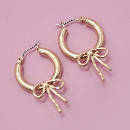 Gold hoop earrings with bow details on a pink background