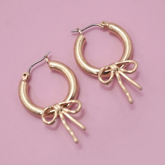 Gold hoop earrings with bow details on a pink background