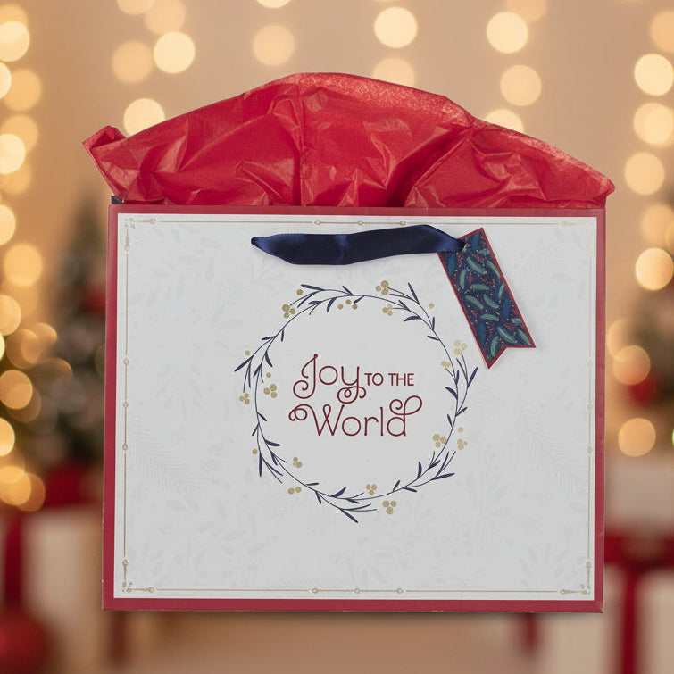 Gift box with 'Joy to the World' text against a festive background with blurred Christmas trees and lights.